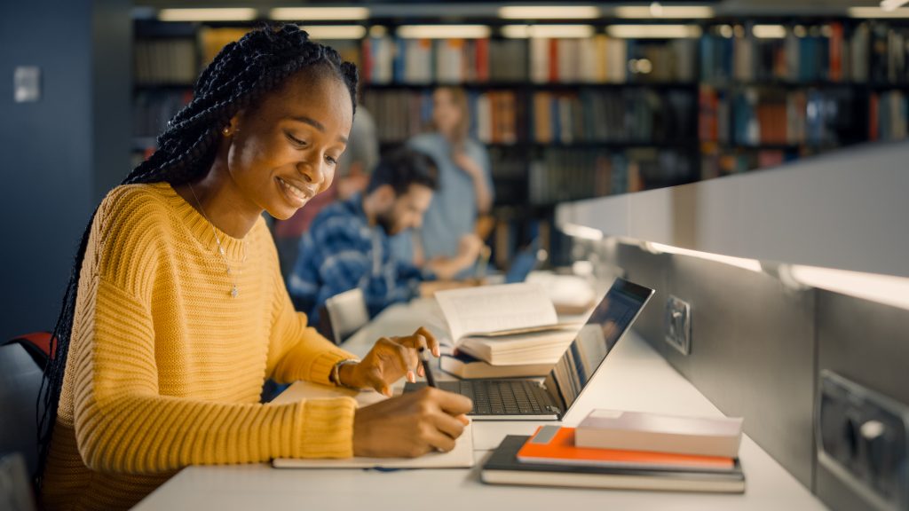 A university student writes in a book in a library.